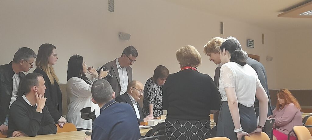 Uczestnicy spotkania ustawieni wokół stołu oglądają zabytkowe monety.