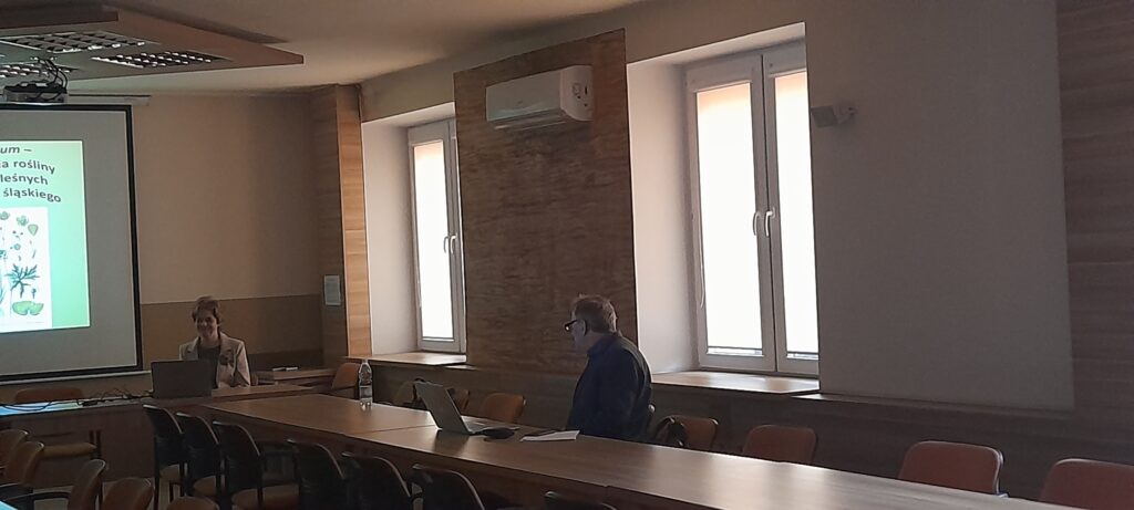 Uczestnik zebrania i prelegentka przy stołach ustawionych w podkowę