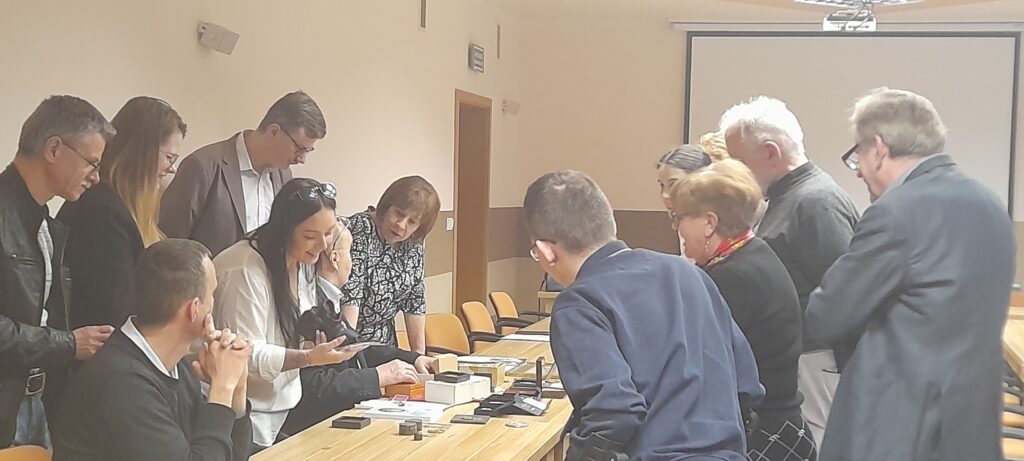 Uczestnicy spotkania ustawieni wokół stołu oglądają zabytkowe monety.