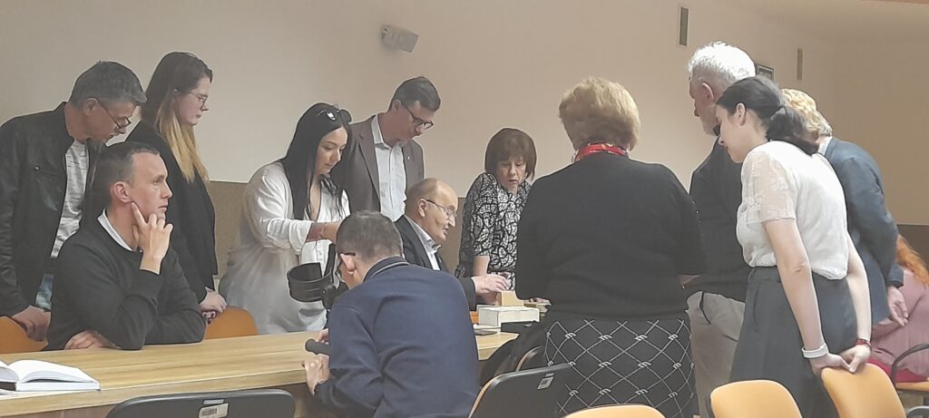 Uczestnicy spotkania ustawieni wokół stołu oglądają zabytkowe monety.
